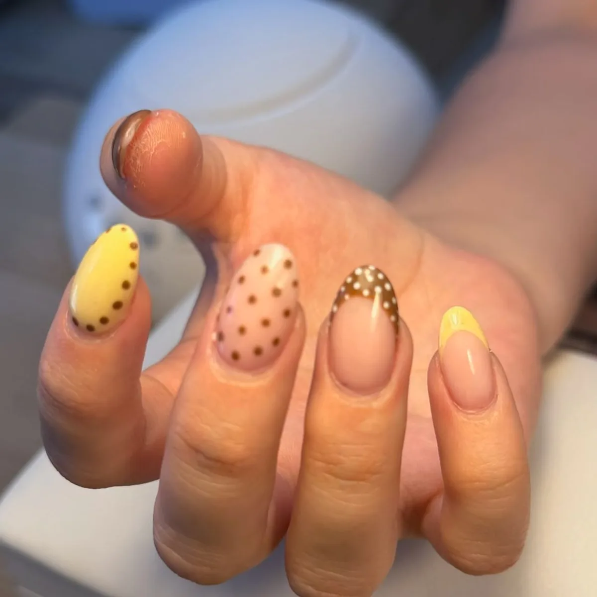 Uñas almendradas en amarillo pastel y nude con topos marrones