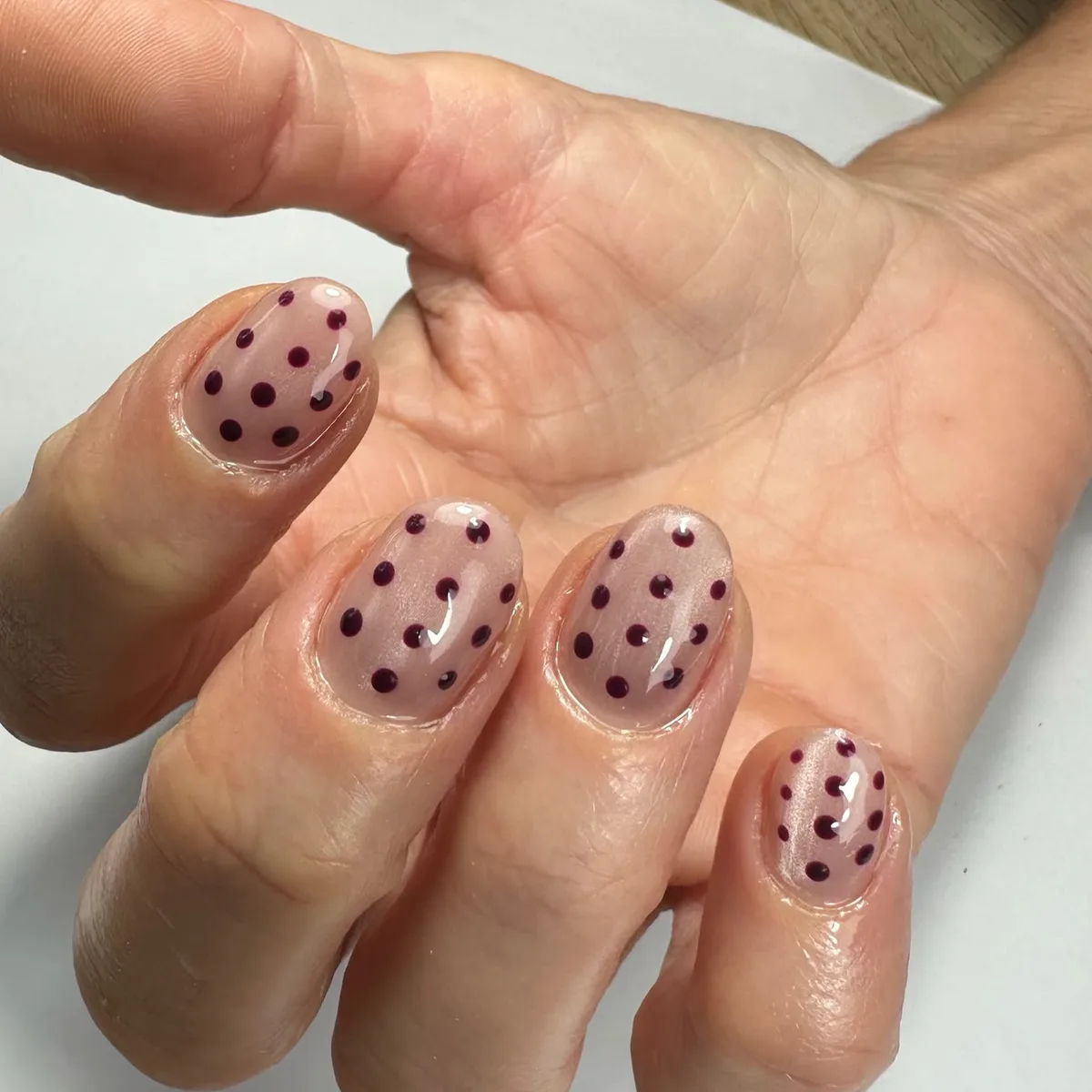 Manicura en uñas cortas ovaladas, base rosa nude con lunares granate